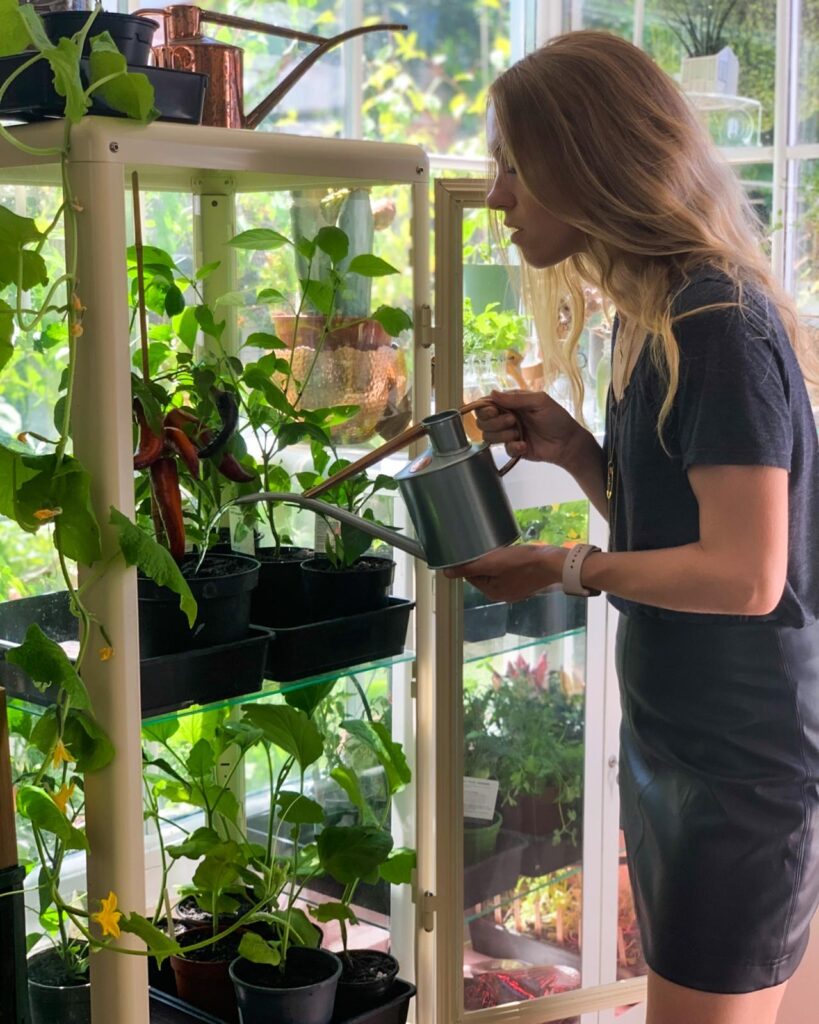 Woman waters her plants which are in pots on a shelf.