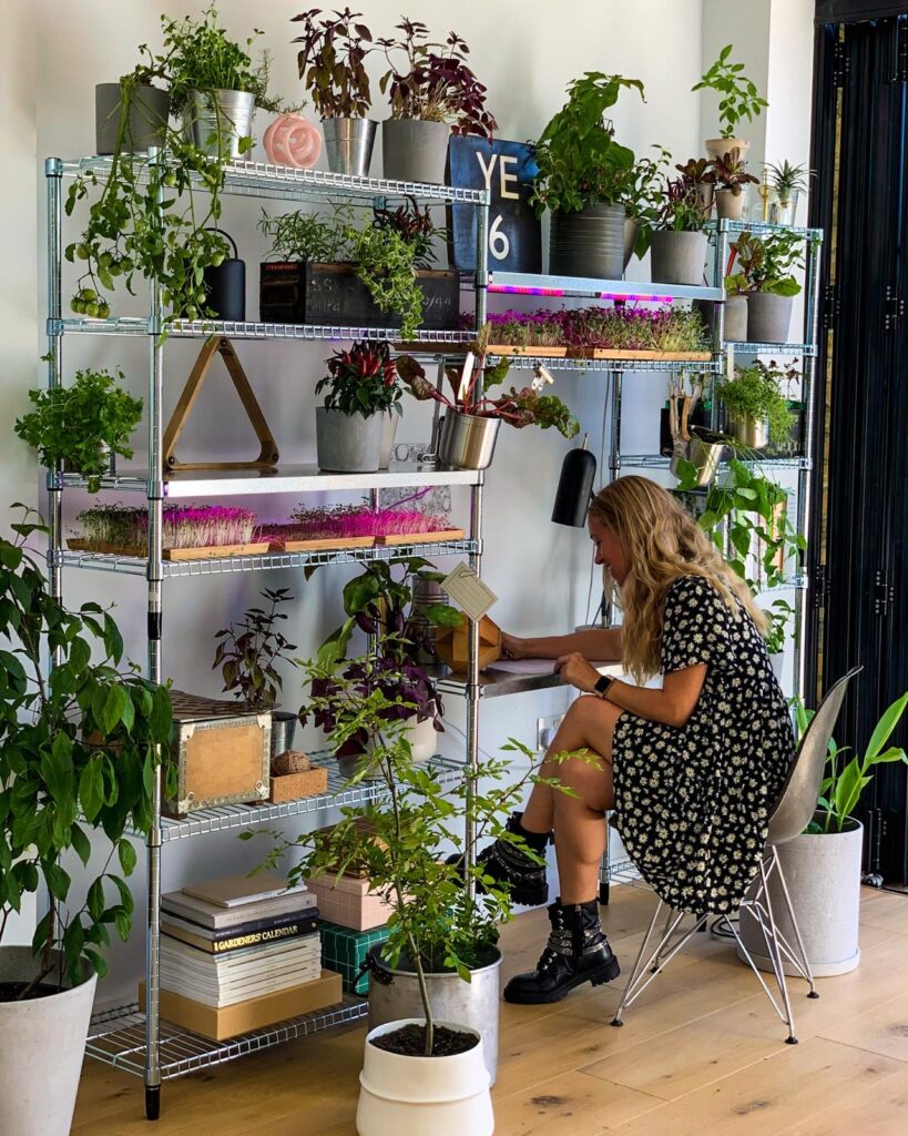 Woman sits amongst her plants in an inside garden.